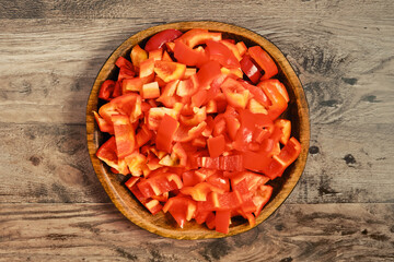 Colorful chopped red bell peppers ready for cooking in a wooden bowl on a rustic table