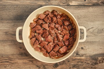 Cooking beef chunks in a large pot on a rustic wooden table for a hearty meal preparation