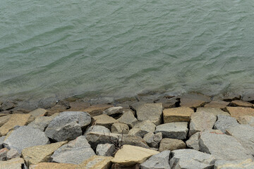 rocky shoreline with gentle water ripples, natural stones meeting calm greenish lake surface, serene outdoor landscape detail with soft textures 