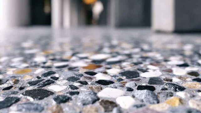 A low-angle close-up shot of a polished aggregate concrete floor with multi-colored stones The background is a blurred interior hallway