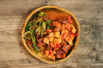 Hearty beef stew served with greens and vegetables in a rustic wooden bowl
