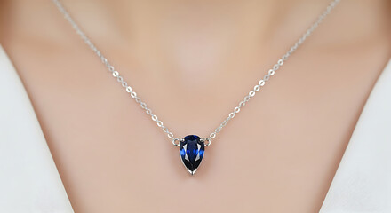 A closeup of a woman wearing a delicate silver necklace with a pearshaped deep blue sapphire pendant resting on her collarbone