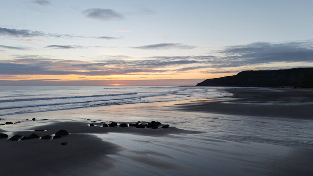 Sunset Serenity &mdash; Cayton Bay Scene with Gentle Waves, Rocky Foreground, and Silhouetted Headland