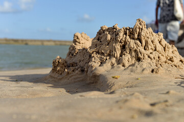small sandcastle on tropical beach, blurred background of river and sky, summer fun concept, close up of handmade sand fort, water and horizon view, childhood memories, detail of rough, cracked wet sa