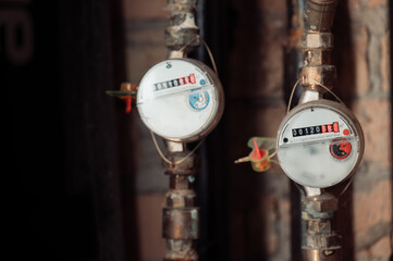 A close-up view of water meters attached to pipes on a brick wall highlighting their design with colored dials and numerical readings showcasing the details of plumbing