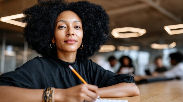 A confident woman with a vibrant curly hairstyle sits at a sunlit table, writing notes and brainstorming ideas. The modern workspace buzzes with collaborative energy