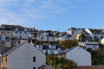 A row of coastal homes are pictured. They are white with black roofs, and are placed on a hillside in Perranporth - Cornwall - UK