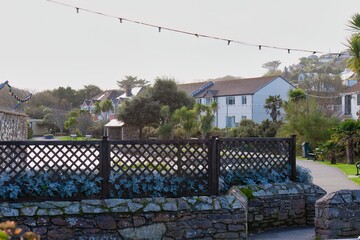 A peaceful view shows a well-kept park with stone walls and a wooden fence, backed by houses on a gentle hil in Perranporth - Cornwall - UK