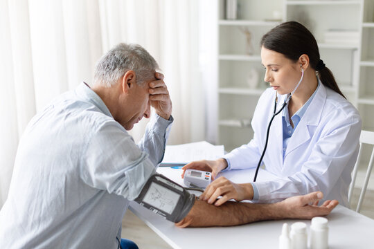 Female doctor checking blood pressure of senior male patient with stethoscope during medical examination in clinic office, professional healthcare service