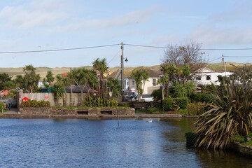 A tranquil pond reflects the homes and verdant landscape beyond, showcasing the serene beauty in Perranporth - Cornwall - UK