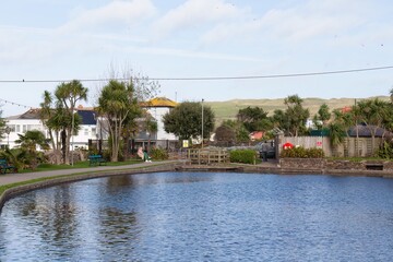 A scenic pond is framed by greenery and buildings under a bright sky in Perranporth - Cornwall - UK
