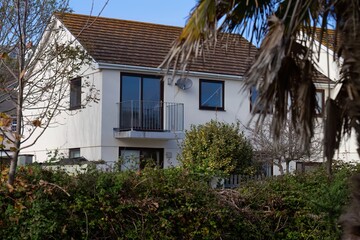 A white house with a brown roof viewed through greenery in Perranporth - Cornwall - UK