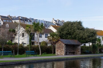 Waterside homes create a peaceful scene. A stone bus shelter sits in the foreground, next to a tranquil waterway in Perranporth - Cornwall - UK