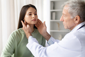 Senior male doctor touching lymph nodes and consulting pregnant woman in clinic, prenatal medical checkup and healthcare examination concept