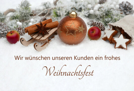 Weihnachtskarte: Winterliche Kulisse mit braunen Christbaumkugeln,Zimtsternen ,&Auml;pfeln und Tannenzweigen im Schnee. Im Schnee steht der Text wir w&uuml;nschen unseren Kunden ein frohes Weihnachtsfest.