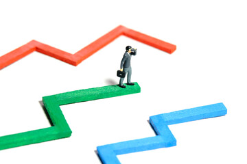 Miniature tiny people toy figure photography. Progress monitoring concept illustration. A businessman using binocular telescope standing above multiple bar chart