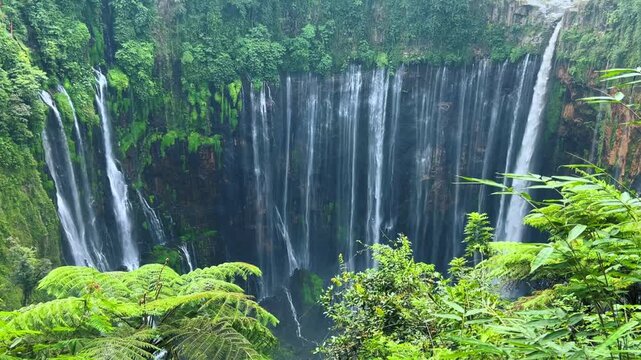 The multi-tiered Tumpak Sewu waterfall, with its lush greenery and wide stream of water flowing into a deep, semi-circular basin on the island of Java. Near Mount Semeru. Indonesia. 4К