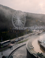The Ferris wheel against the backdrop of misty mountains and busy traffic.