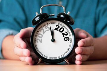 Businessman holding an alarm clock showing the transition from 2025 to 2026 symbolizing time change...