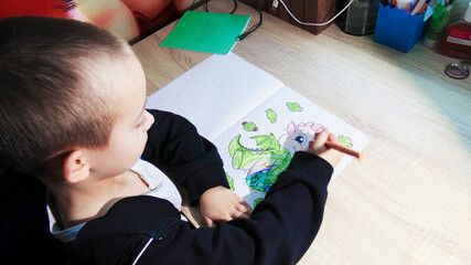 A young child with short hair colors a cartoon character in a coloring book using orange crayons....