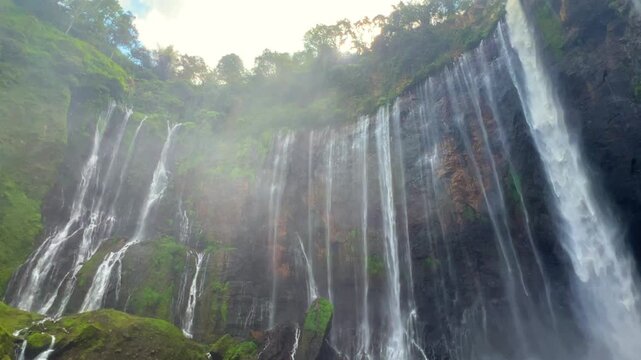 The multi-tiered Tumpak Sewu waterfall, with its lush greenery and wide stream of water flowing into a deep, semi-circular basin on the island of Java. Near Mount Semeru. Indonesia. 4К