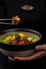 A girl uses chopsticks to take a piece of food from a poke bowl