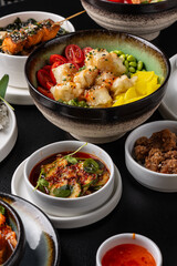 A large table with Asian cuisine. Soups, sushi, appetizers, poke bowls, shrimp, sauces