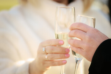 A romantic close-up of a couple clinking champagne glasses, both wearing wedding rings. The focus is on their hands and sparkling wine, suggesting celebration or engagement.