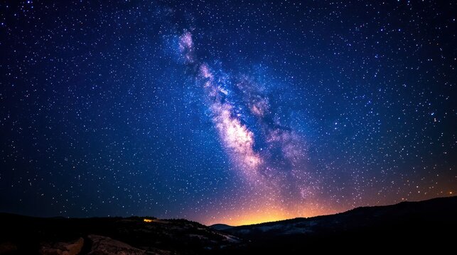 A starry night sky with the Milky Way galaxy visible in the distance, illuminated by the glow of distant stars and the moon's light, with a silhouette of a mountain range in the foreground.