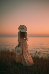 Woman with long dress holding a sunhat facing sea horizon