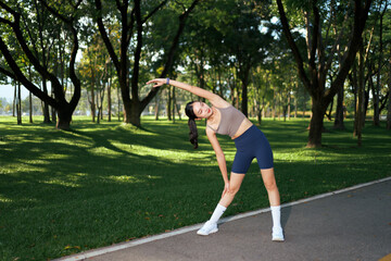 Woman exercising outdoors, stretching body in green park