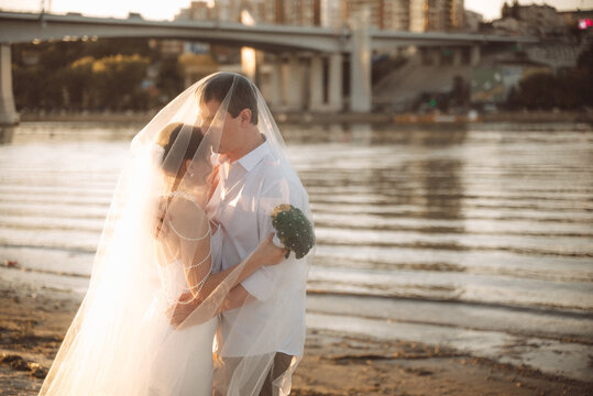 Romantic couple embracing on the beach, bride in veil holding broccoli bouquet, groom in white shirt, seaside wedding moment