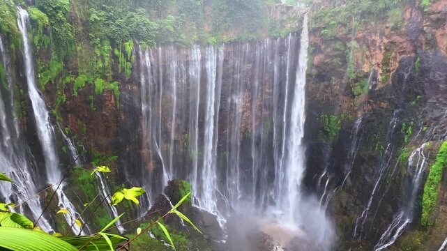 The multi-tiered Tumpak Sewu waterfall, with its lush greenery and wide stream of water flowing into a deep, semi-circular basin on the island of Java. Near Mount Semeru. Indonesia. 4К