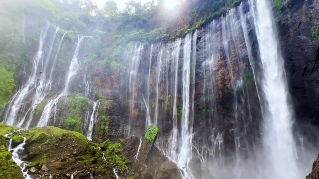 The multi-tiered Tumpak Sewu waterfall, with its lush greenery and wide stream of water flowing into a deep, semi-circular basin on the island of Java. Near Mount Semeru. Indonesia. 4К	
