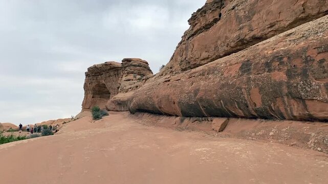 Hiking the trail to Delicate Arch in Arches National Park at dusk, warm evening light casts long shadows over the red rock landscape.