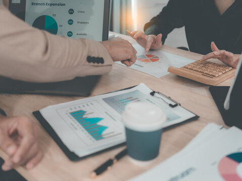 A statistician is preparing charts and documents for a meeting. A team of professionals is reviewing financial documents. Pointing to charts on the desk. Working. - Powered by Adobe