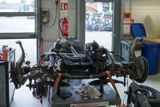 A detailed view inside a professional auto repair workshop showing a car front subframe with suspension, steering, and drivetrain components placed on a workbench