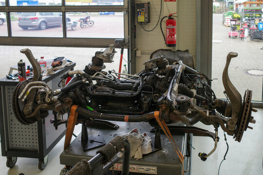 A detailed view inside a professional auto repair workshop showing a car front subframe with suspension, steering, and drivetrain components placed on a workbench