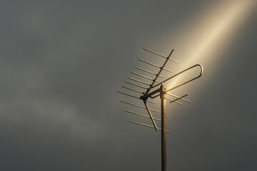 An old TV antenna in a beam of soft light against the sky. Space for text.