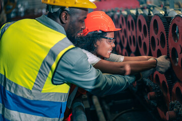 Female engineer hand trap in big machinery gears factory accident. Male colleague help, demonstrate quick response teamwork. Both wear safety helmet and vest,Industrial workplace,emergency, assistance