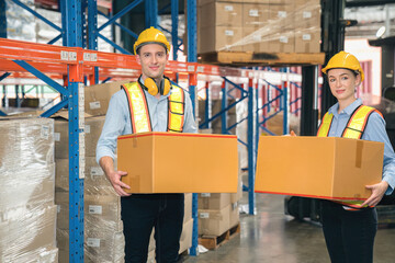 White Man and woman warehouse worker wear safety helmets, safety vests carry cardboard box in industrial factory storage inventory. Show teamwork efficient modern logistics, supply chain management