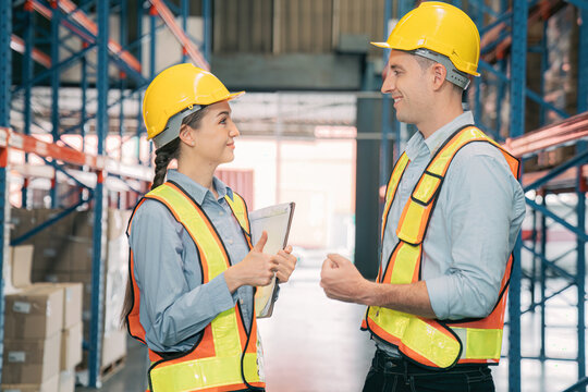 Confidence caucasian man, woman staff worker wear safety helmets, vest show teamwork collaborate, cooperation in logistics inventory operation. show success, efficiency in modern warehouse management.