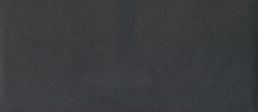 Black rough surface of old paper or cardboard, background, texture. Backdrop of black paper surface with elements of aging. Old and shabby paper piece. Ancient wall in ashen color. Black paper surface