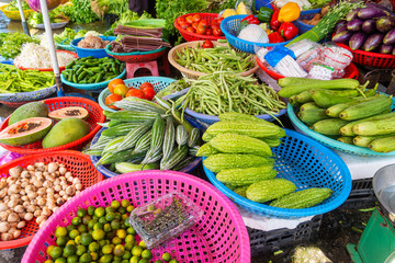 Colorful display of assorted fresh vegetables and fruits in plastic baskets at traditional food market in Phu Quoc, Vietnam. Bitter melons, cucumbers, long beans, papaya, eggplants, limes, mushrooms