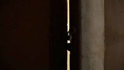 Padlock and keys hang on a dark wooden door slightly ajar, revealing a bright crack of light. Mysterious, hidden access, or secret reveal concept.