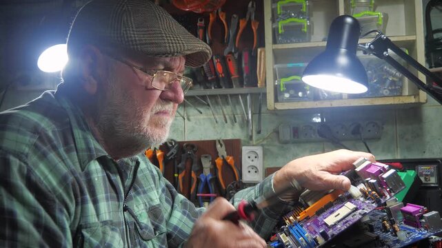 An elderly technician repairs computer equipment in a workshop using measuring instruments and technical tools. Slow motion.