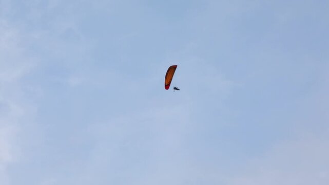 A motorized paraglider (paramotor/powered parachute) flies across a cloudy sky, towing a white advertising banner. Recreation, extreme sport, and aerial advertising activity.