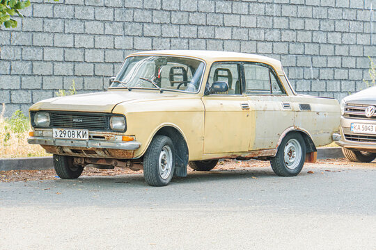 An older compact vehicle two doors, hardtop parked on a road with a stone wall backdrop Car appears weathered due to chipped and faded paint - Kyiv, Ukraine 07-04-2025