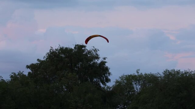 A motorized paraglider (paramotor/powered parachute) flies across a cloudy sky, towing a white advertising banner. Recreation, extreme sport, and aerial advertising activity.