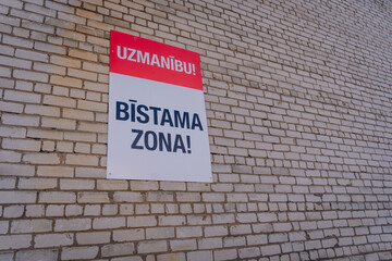 Fototapeta premium Warning sign on a brick wall indicating a restricted area, featuring bold text and a vibrant color scheme, emphasizing safety and caution in the environment